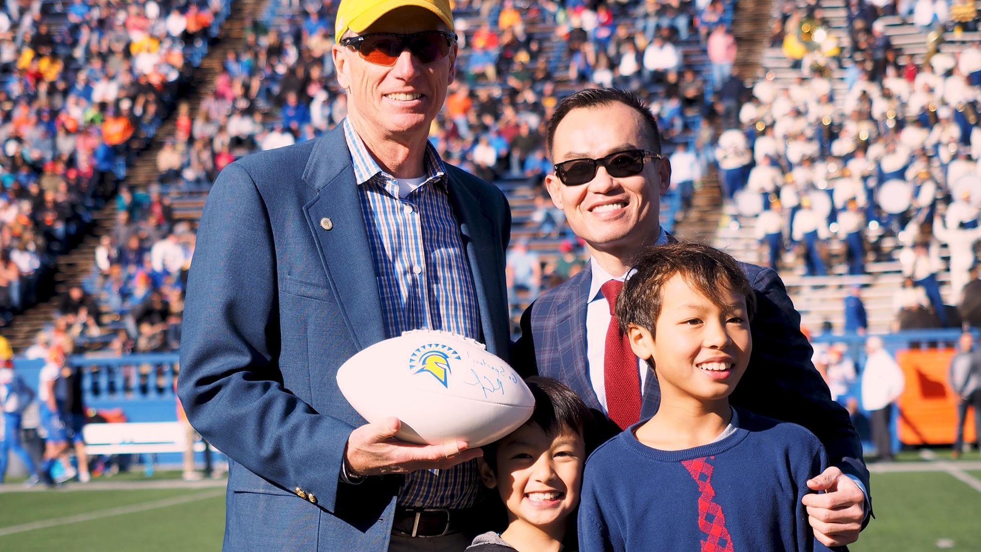 A father with his two young boys next to a tall man holding a football